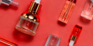 Assorted dropper bottles with gold and white caps on a red background arranged in a flat lay pattern