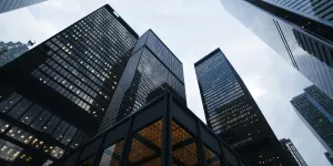 Low-angle view of modern skyscrapers with glass facades under a cloudy sky in an urban cityscape.