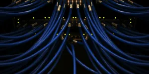 Close-up of blue network cables plugged into a switch with glowing yellow indicator lights in a server room.