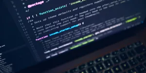Close-up of a laptop screen showing colorful programming code and keyboard in low light.