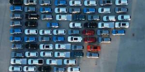 Aerial view of multiple cars in organized rows on a concrete lot, featuring various colors and models.