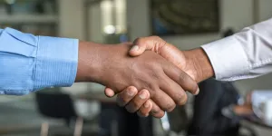 Close-up of two people shaking hands in an office setting, symbolizing agreement and partnership.