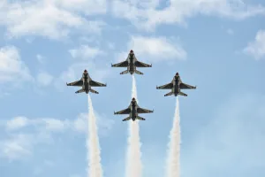 Four fighter jets flying in tight formation leaving white smoke trails against a blue sky with clouds.