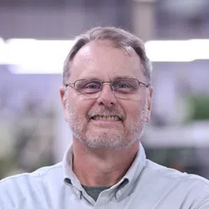 Smiling middle-aged man with glasses and a beard wearing a light shirt in a bright indoor setting
