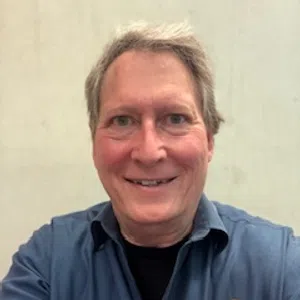 Smiling man wearing a blue Thermal Economy Inc uniform shirt against a plain light background.
