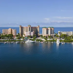 Aerial view of waterfront condos and yachts docked along the marina under a clear blue sky.
