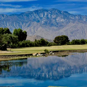 Mountain landscape reflected in a serene lake next to a golf course under a clear blue sky