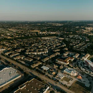 Aerial view of a sprawling suburban neighborhood with residential buildings, roads, and parking areas under clear sky.
