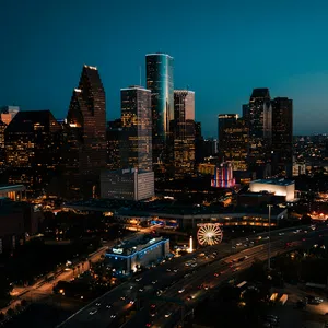 Nighttime cityscape of Houston featuring illuminated skyscrapers, highways, and a lit Ferris wheel.