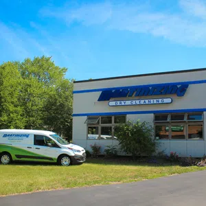 Martinizing Dry Cleaning storefront and branded service van parked on grass under a clear blue sky.