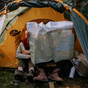 Two campers sitting in front of a tent surveying a large printed map