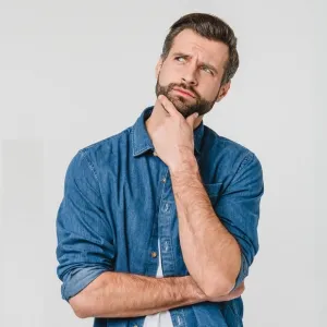 Man with beard and denim shirt thoughtfully looking up with hand on chin