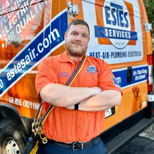 Technician in orange Estes Services uniform stands with arms crossed by branded service van with overlaid text.