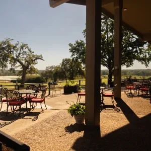 Outdoor patio with wrought iron tables and red chairs overlooking green landscape and trees on a sunny day