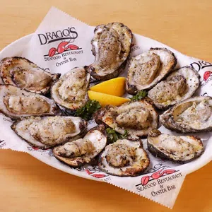 Grilled oysters on a white plate with lemon wedges, served on branded paper from Drago's Seafood Restaurant.
