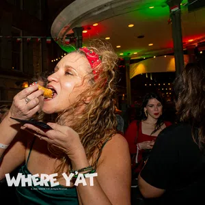 Woman in red headband eating fried food at lively nighttime party with people drinking and socializing.