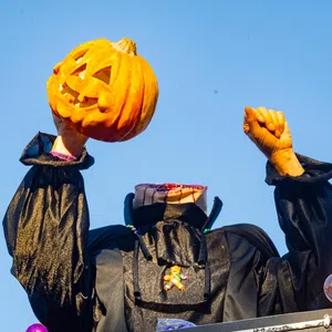 Headless Halloween figure in black costume holding a carved pumpkin against a clear blue sky.