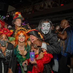 Group of adults in colorful and creative costumes posing indoors at a lively Halloween or costume party.