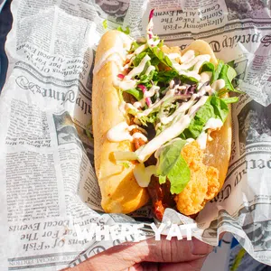 Fresh fried fish sandwich with lettuce and sauce served in newspaper-style wrapping held by a person.
