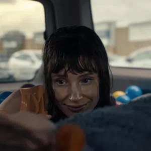 Woman with wet hair smiling inside a car filled with colorful plastic balls, looking at someone out of focus.
