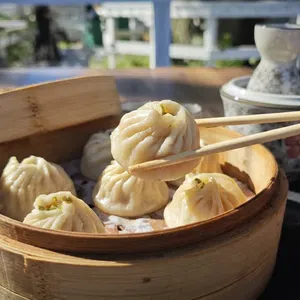 Chopsticks picking up a steamed dumpling from a bamboo basket on a wooden table outdoors