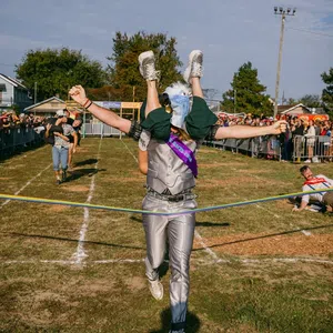 Person in eagle costume winning a race while carrying another runner across the finish line at outdoor event.