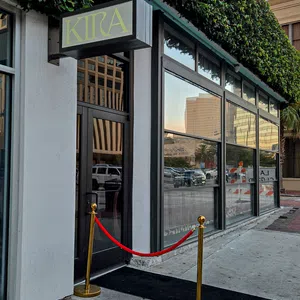 Entrance to KIRA with black door, red velvet rope, gold stanchions, and green ivy on urban building facade.