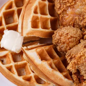 Crispy fried chicken pieces served with golden waffles and a dollop of melting butter on a white plate.