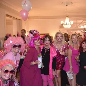 Group of women dressed in pink and black at an indoor party with balloons and drinks celebrating together.