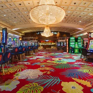 Colorful casino interior with floral carpet, gaming machines, blue chairs, and large chandeliers overhead