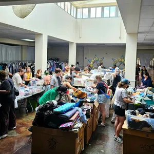 Volunteers sorting and organizing clothing donations in a large, well-lit community center with boxes and racks of clothes.