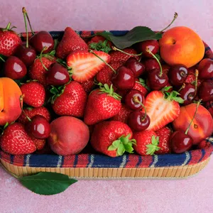 Basket filled with fresh strawberries, cherries, peaches, and apricots on a pink surface