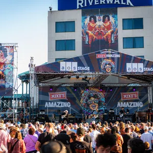 Outdoor music festival on Mike's Amazing stage at Riverwalk with large crowd enjoying live band performance.