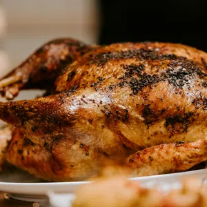Golden-brown roasted whole chicken with herbs on a white plate ready to serve.