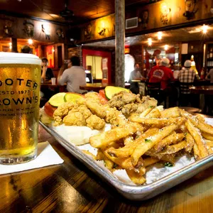 Fried seafood platter with fries and a cold beer glass on a wooden table in a cozy bar setting.