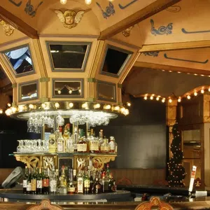 Elegant vintage bar interior with ornate ceiling, lights, central liquor display, and wooden chairs under warm lighting.