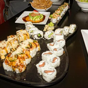Assorted sushi rolls with sauces and garnishes served on a black platter and white plates on a dark table.