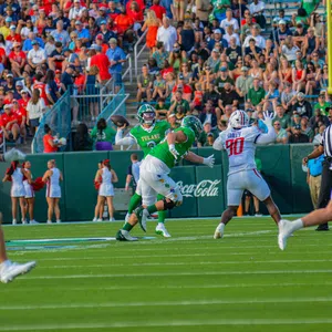 Tulane quarterback prepares to throw under pressure from defenders with crowd and cheerleaders in background