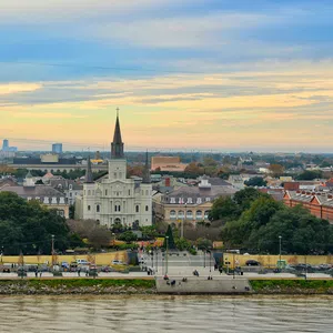 Stunning view of St. Louis Cathedral and Jackson Square with the Mississippi River in the foreground at sunset.
