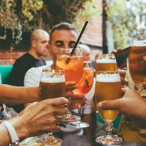 Group of friends clinking glasses with beer and cocktails at an outdoor social gathering.