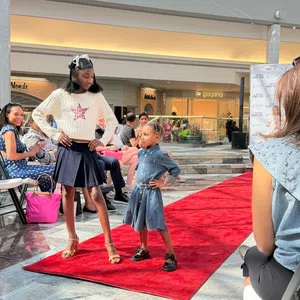 Two young models confidently posing on a red carpet runway during a fashion event in a shopping mall.