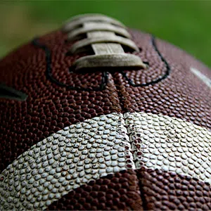 Close-up of a textured brown and white American football showing laces and pebbled surface detail.