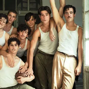 Group of eight young men wearing white tank tops and beige pants posing closely in a vintage room near open windows