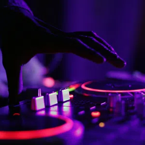Close-up of a DJ's hand adjusting controls on a colorful illuminated mixer in a dark room.