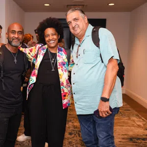 Three diverse adults smiling and posing together indoors at a social event in a hallway.