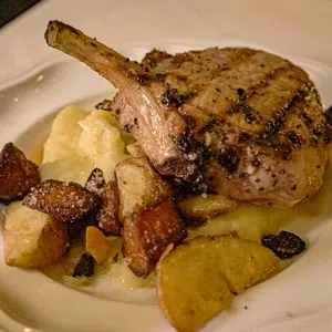 Grilled pork chop with mashed potatoes and roasted root vegetables on a white plate.