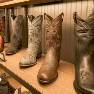 Row of six cowboy boots in various shades displayed on a wooden shelf against a paneled wall.