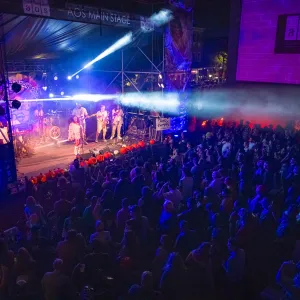 Live band performing on AOS Main Stage with colorful lights and large crowd at night concert event.