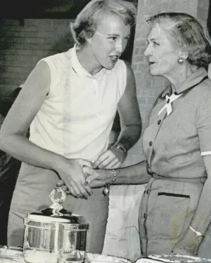 Black and white photo of young woman receiving trophy and handshake from older woman at award ceremony