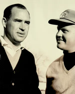 Sepia photo of two men in sweaters, one wearing a cap with the number 22, engaged in conversation outdoors.